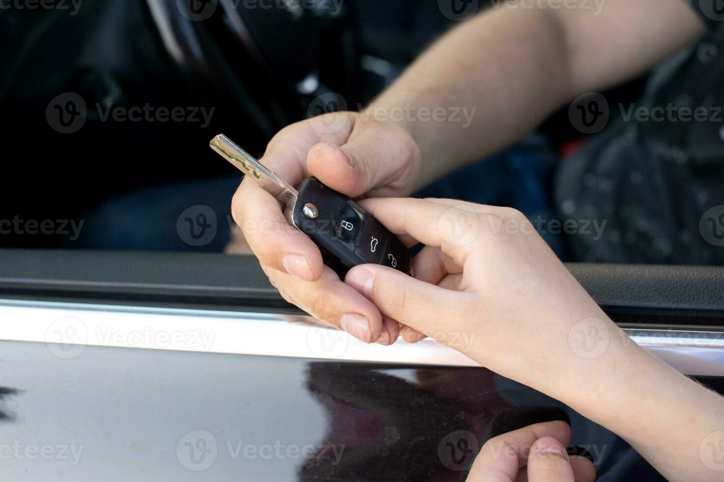 The child holds the car key in his hands. Dad gave his son the car keys. Dad is sitting in the car photo