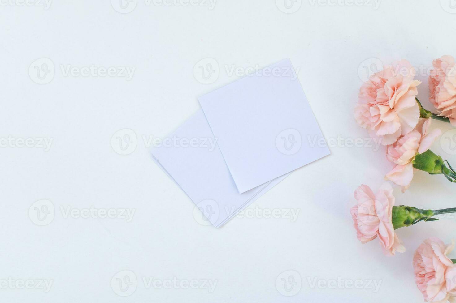 White sheets of stickers for notes lie on a white table with carnation flowers. Space for text photo