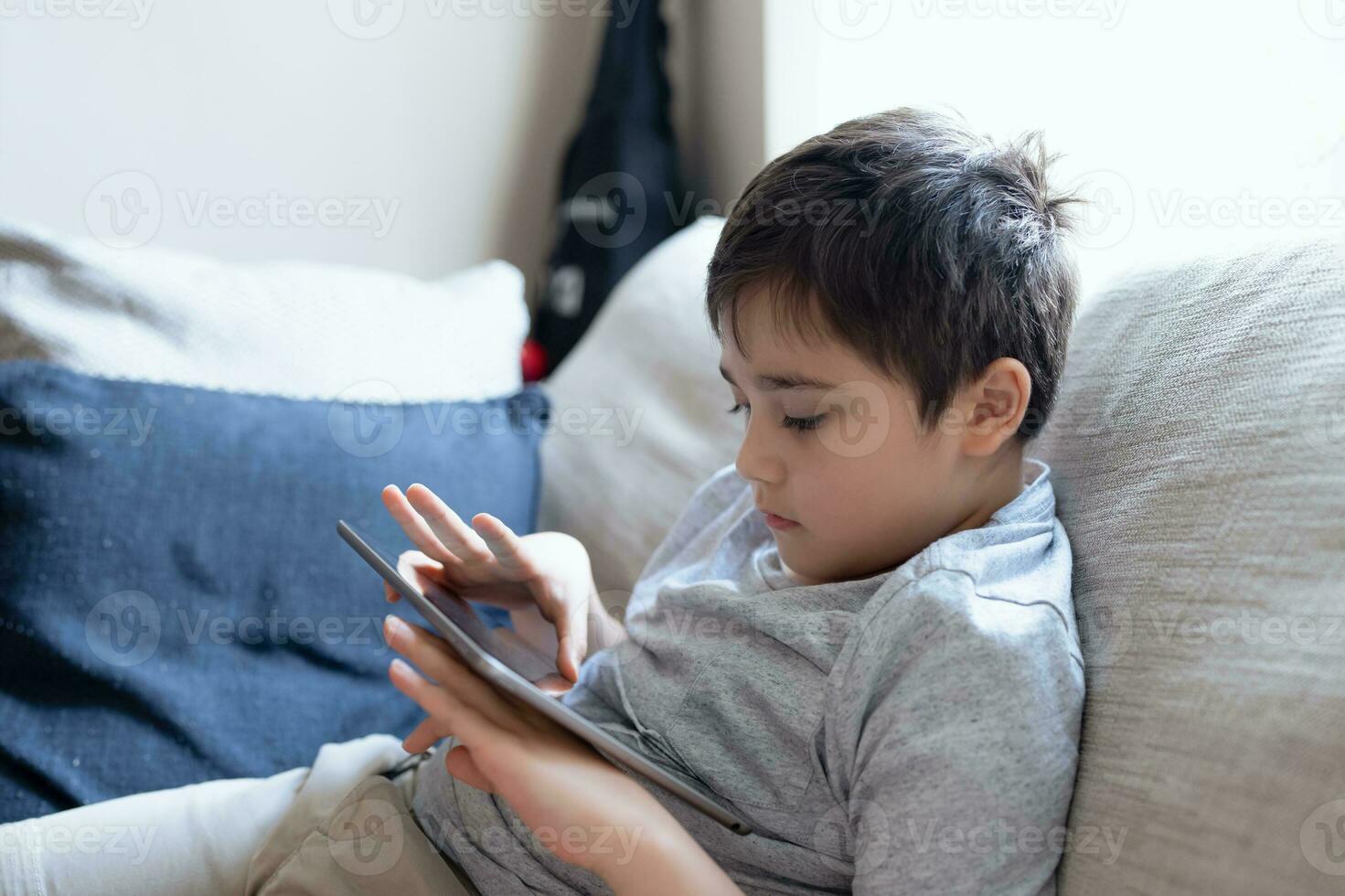 Preteen schoolboy doing homework with digital tablet in living room,Child using gadgets to study. Kid learns online from home,Education learning with new technology for kids. photo
