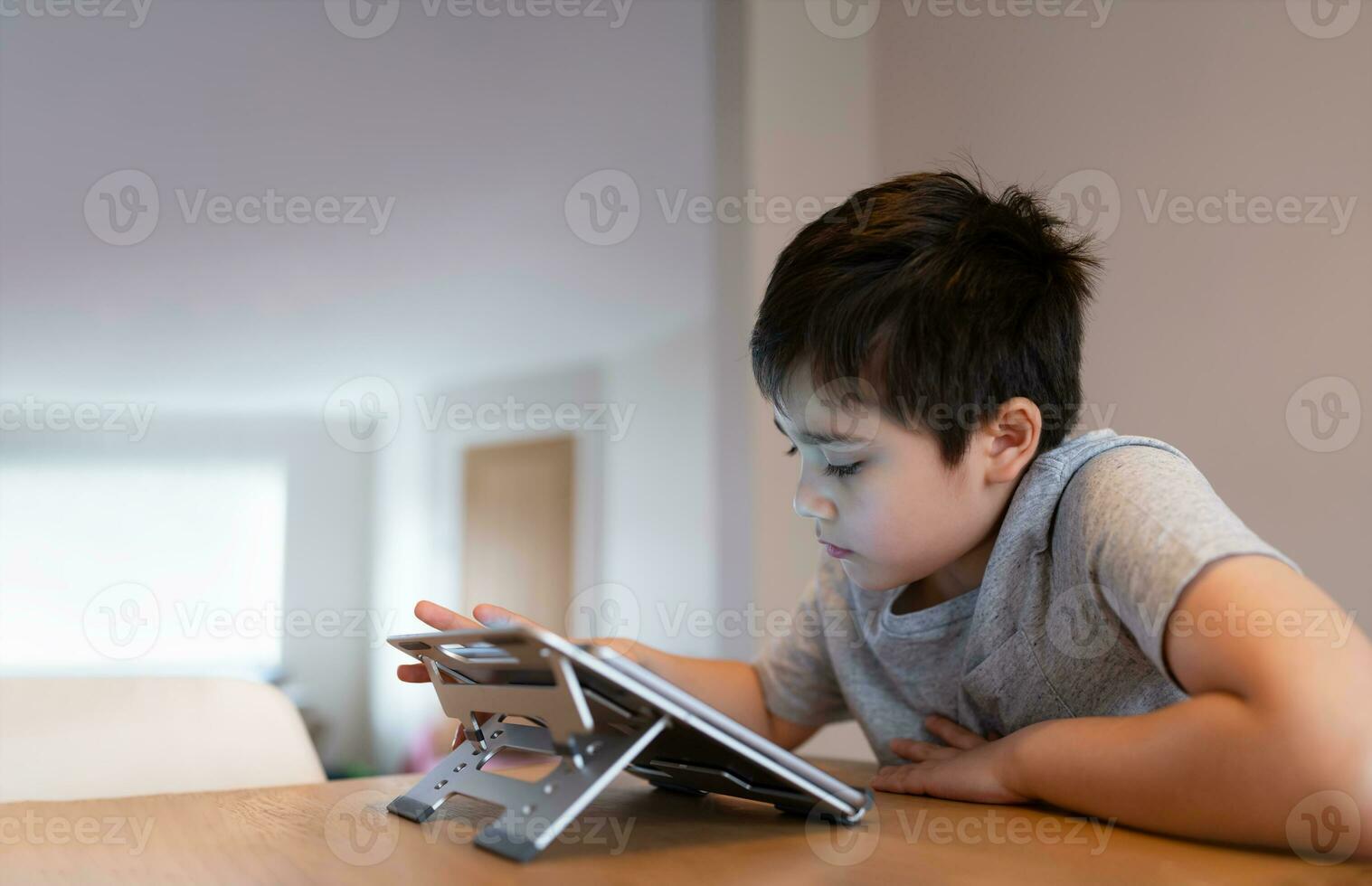 Preteen schoolboy doing homework with digital tablet in living room,Child using gadgets to study. Kid learns online from home,Education learning with new technology for kids. photo