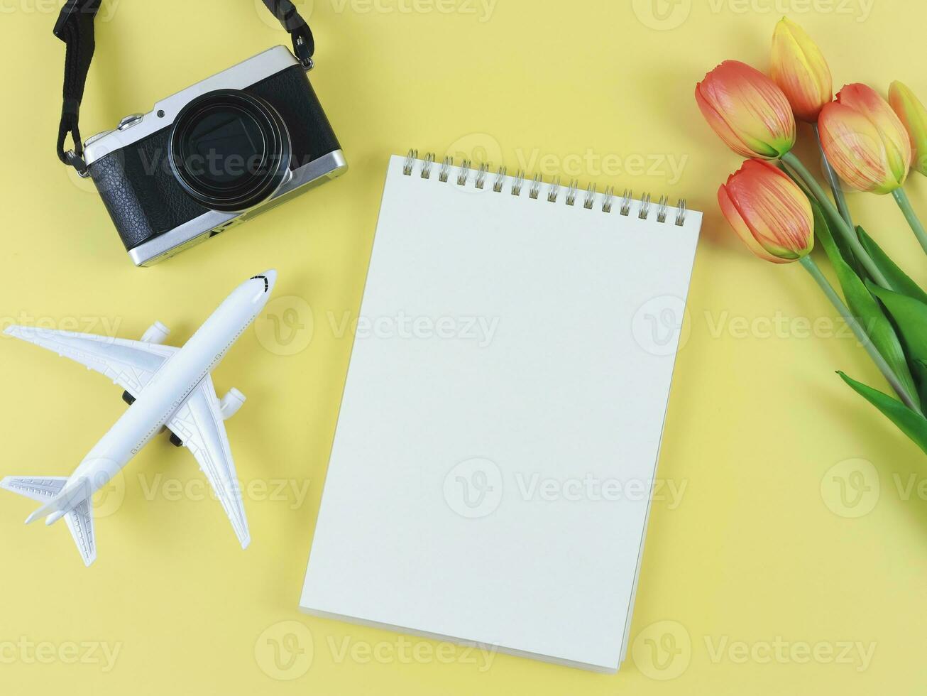 flat lay of blank page opened notebook, airplane model, digital camera and tulips flowers  on yellow  background with copy space. photo