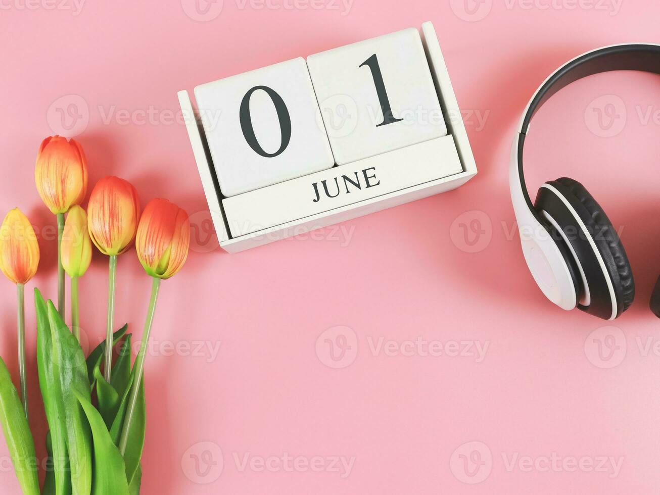 flat lay of wooden calendar with date June 01, headphones and  orange  yellow tulips on pink background, copy space. photo