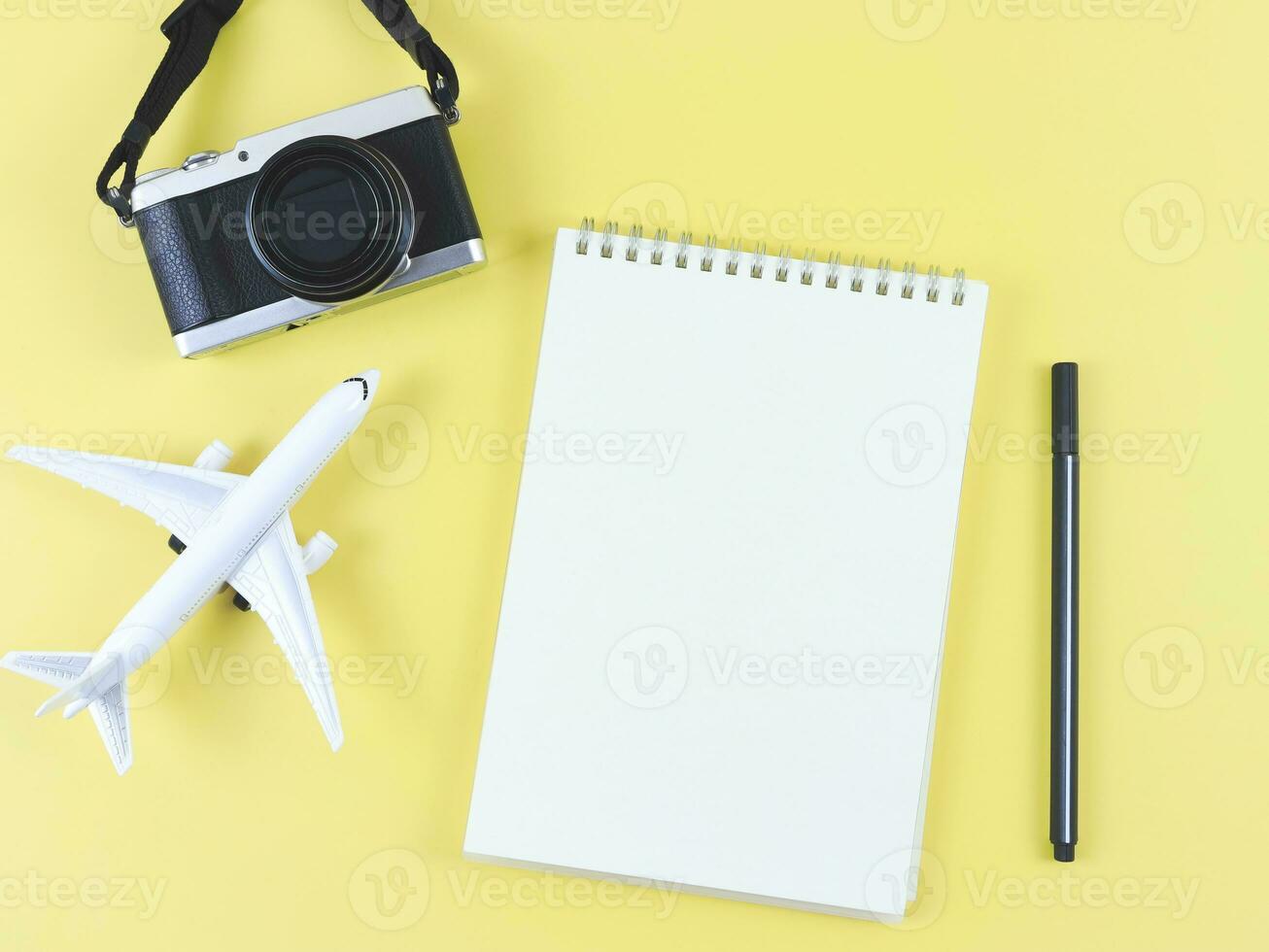 flat lay of blank page opened notebook with pen, airplane model and digital camera on yellow  background with copy space. photo