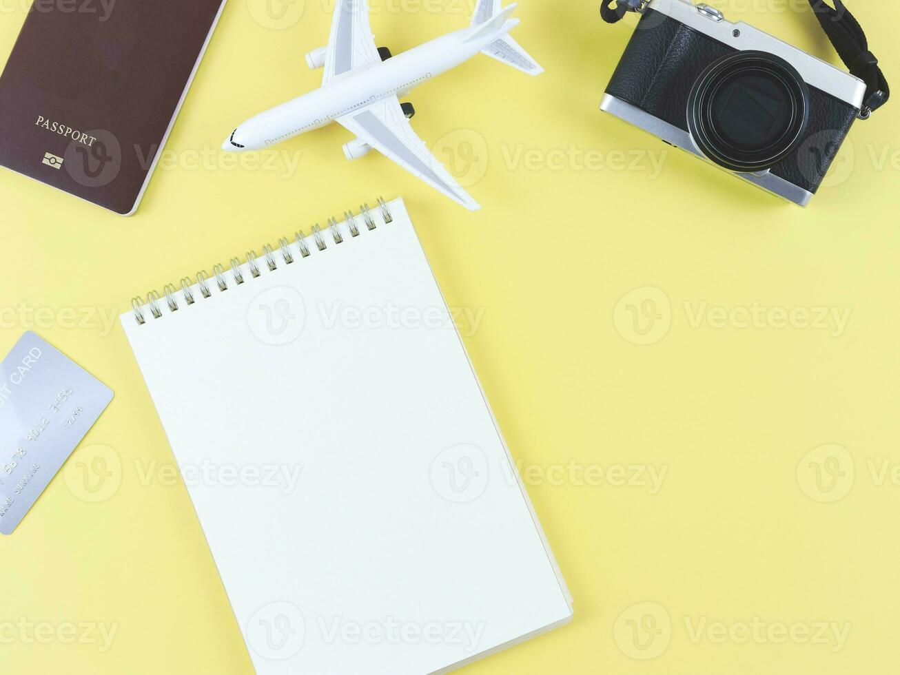 flat lay of blank page opened notebook, airplane model, passport, credit card and digital camera on yellow  background with copy space. photo