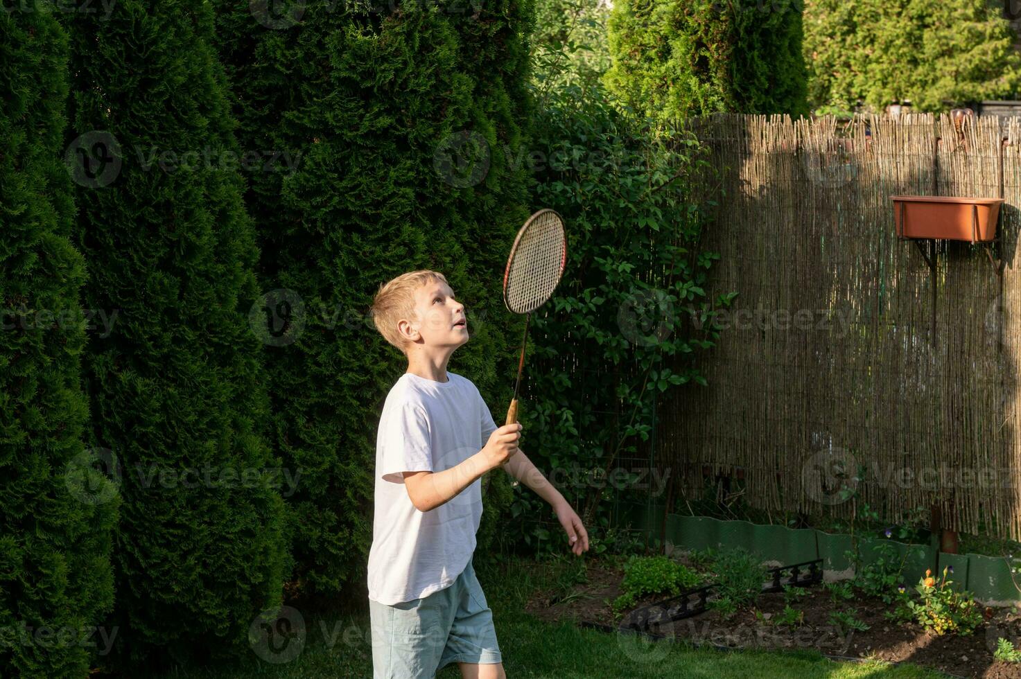 A happy boy holds a badminton racket in his hands, playing sports outside in summer photo