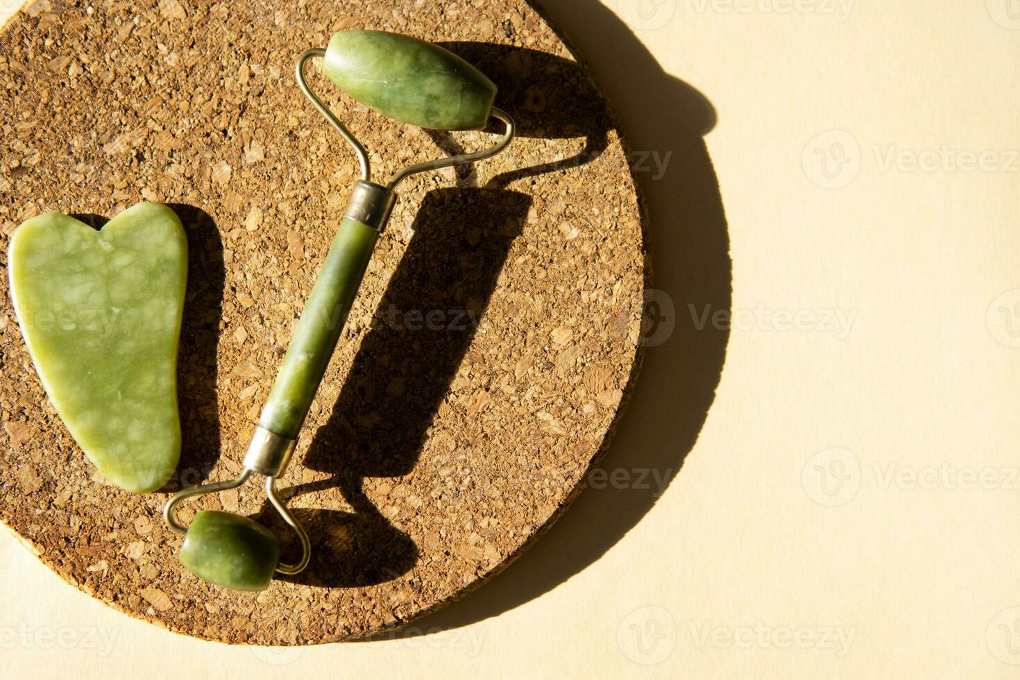 Jade Gua sha scraper and face roller massager on a cork round stand with a monstera leaf. photo