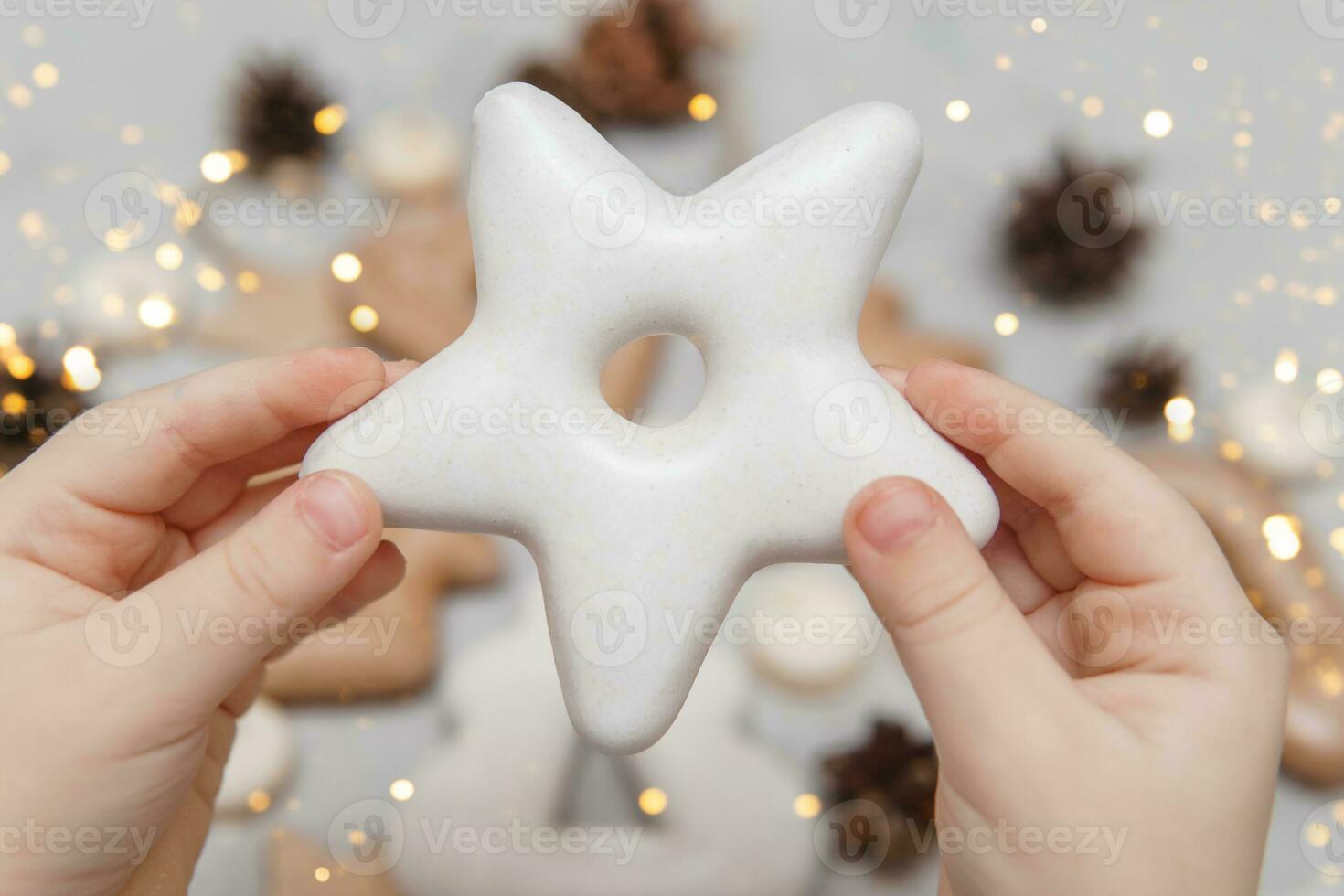 Children's hands hold a gingerbread in the shape of a star. The concept of Christmas sweets, toys, garlands and bokeh. Decor for New Year holidays. photo