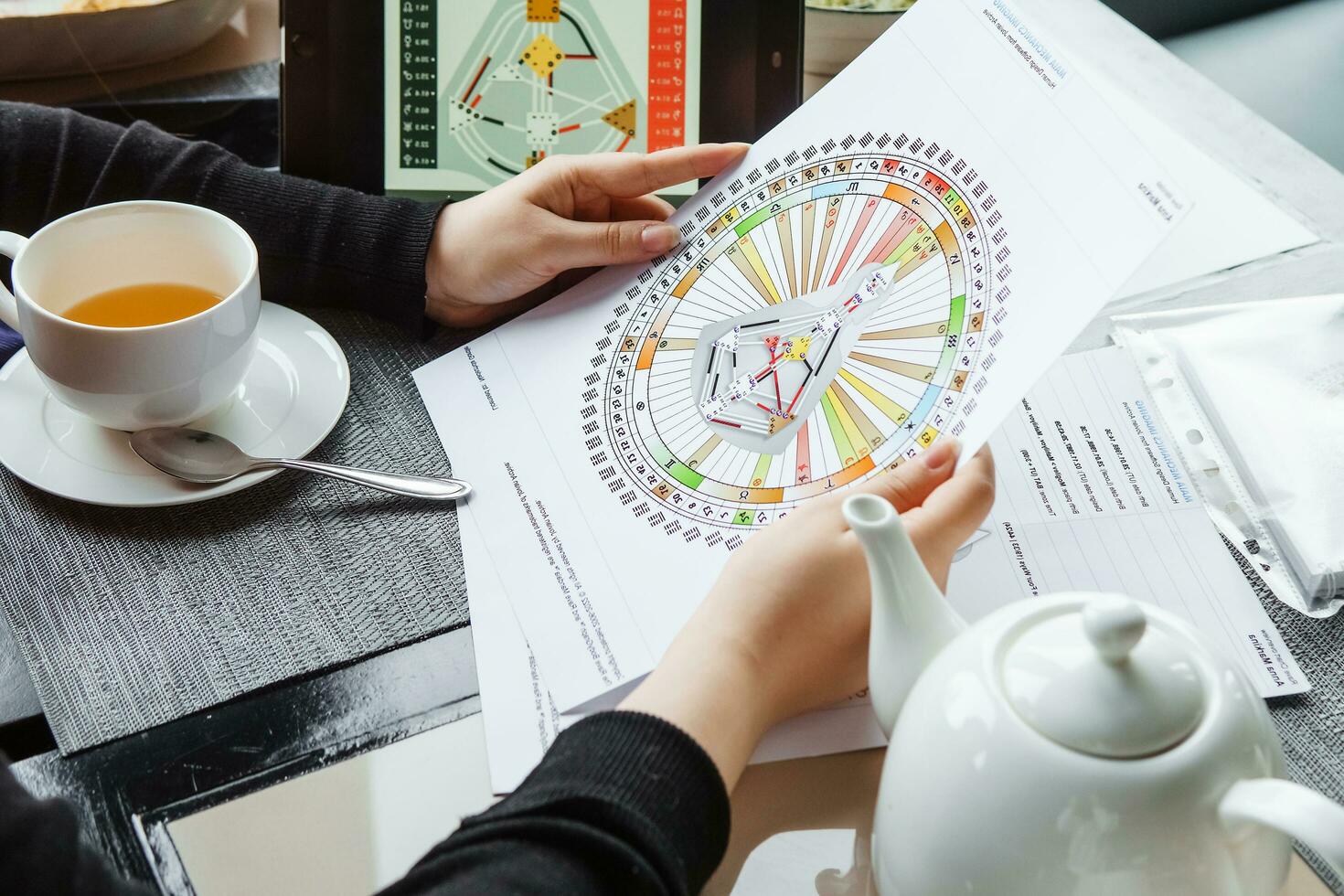 TVER, RUSSIA - FEBRUARY 12, 2023 A woman at the table is studying a rave mandala by human design. Rave mandala on the table close-up. The concept of esoteric teachings. photo