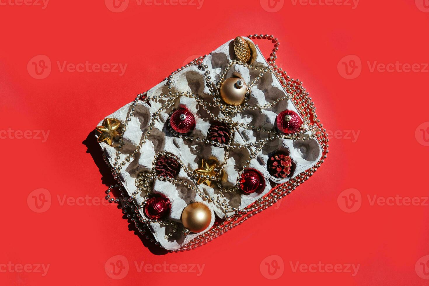 Christmas tree toys in the egg tray on a red background. Top view. The concept of New Year's holidays and Christmas. Red and gold colors. photo