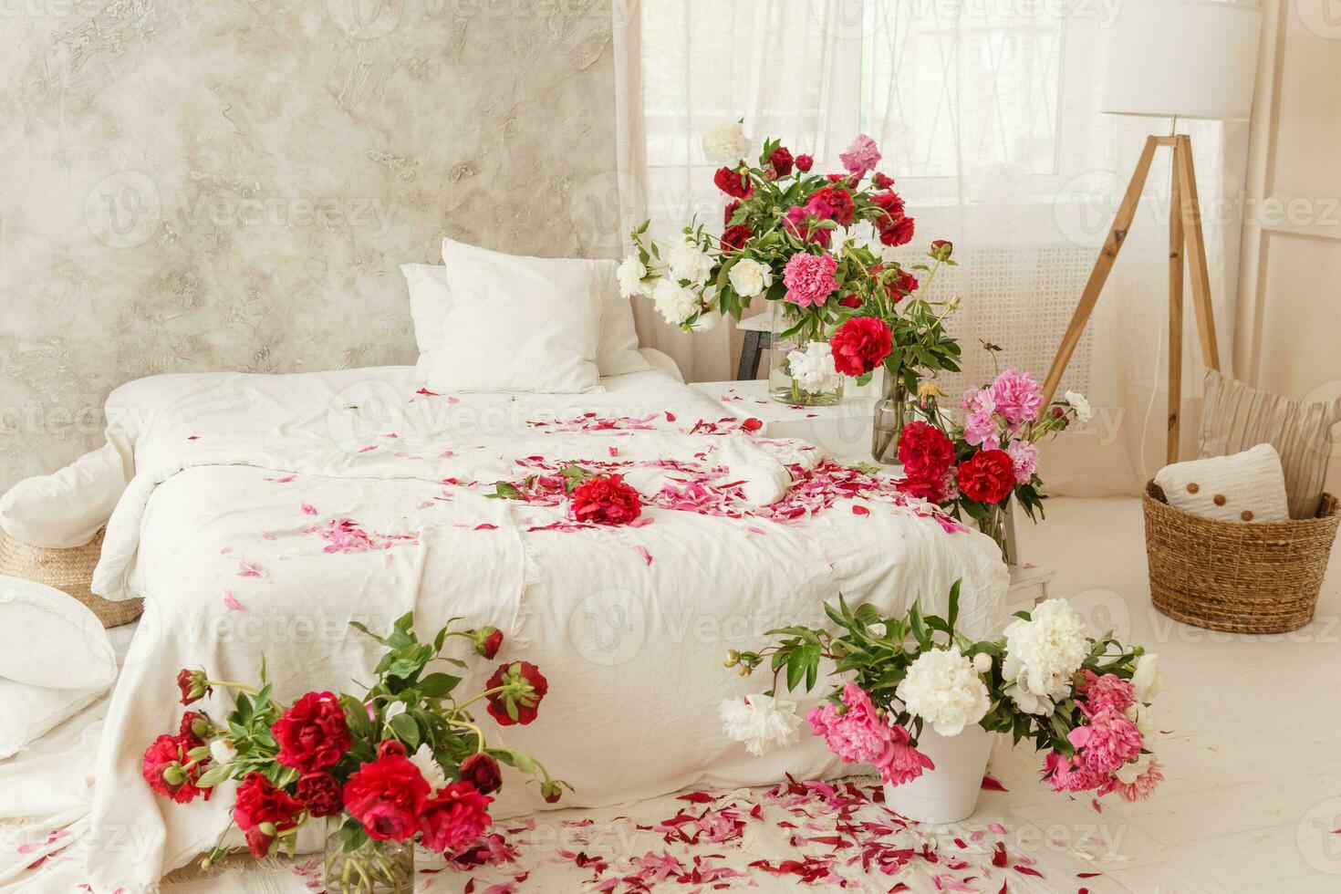 Large white bed in a bright room decorated with vases of bright peonies. Bedroom interior decorated with spring pink flowers. photo