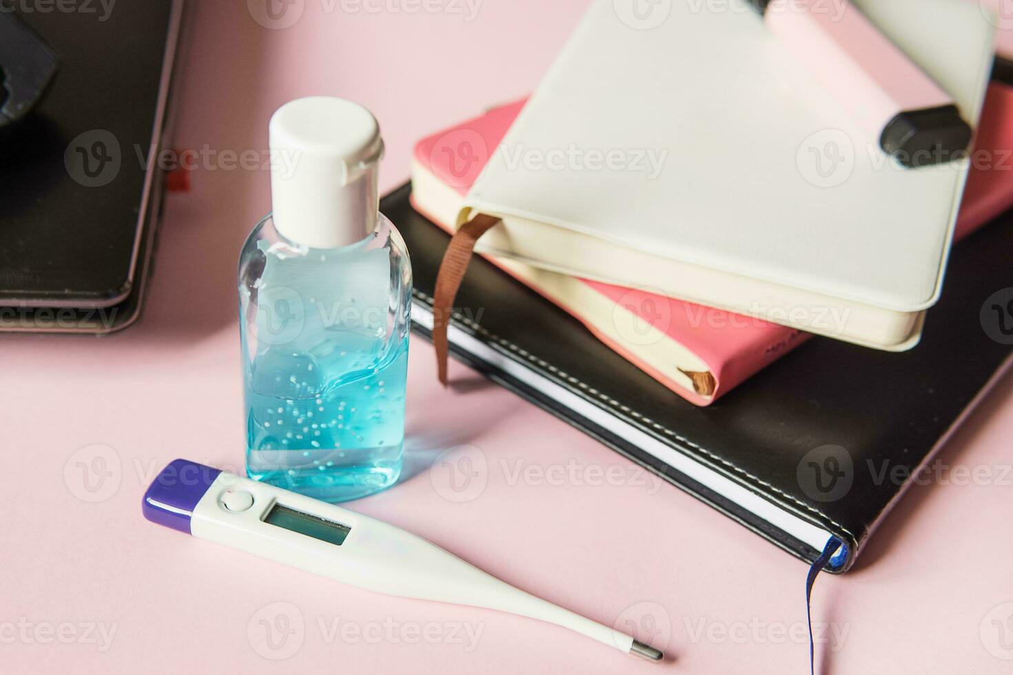 On the desktop, a close-up of a thermometer and hand gel, as well as notebooks, a marker and a laptop. Work from home using an online device protection from coronavirus during the quarantine period. photo