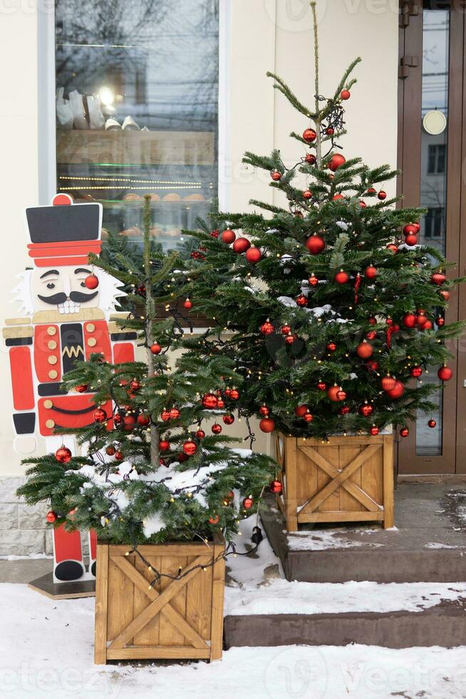 Christmas trees decorated with red balloons in front of the entrance to the cafe. Street Christmas decorations. Christmas trees and a wooden nutcracker photo