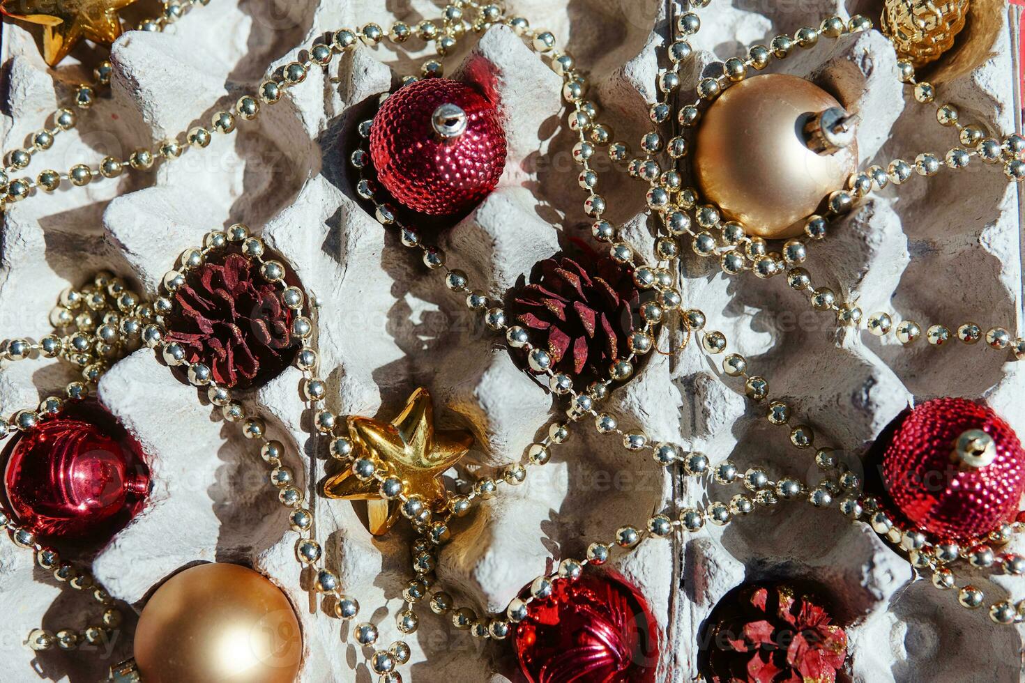 Christmas tree toys in the egg tray on a red background. Top view. The concept of New Year's holidays and Christmas. Red and gold colors. photo