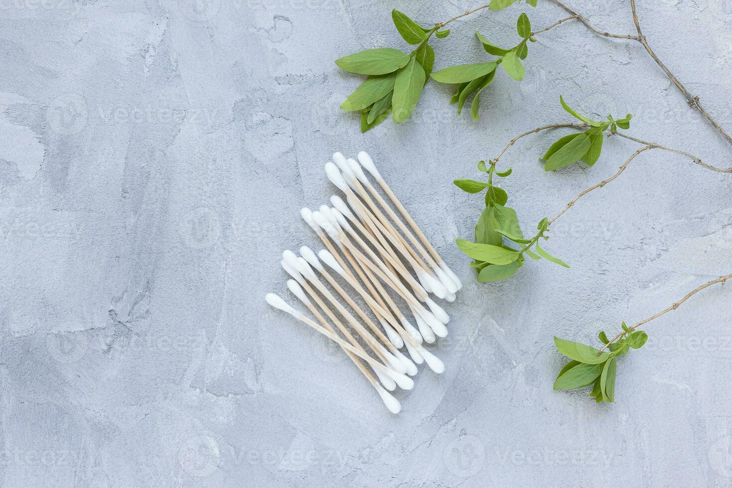 Eco-friendly bamboo cotton buds on gray background, green leaves. Cotton swabs, ear cleaner sticks photo