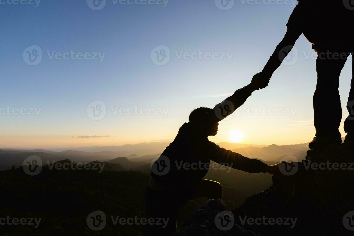 Silhouettes of two people climbing on mountain and helping. Help and assistance concept. photo