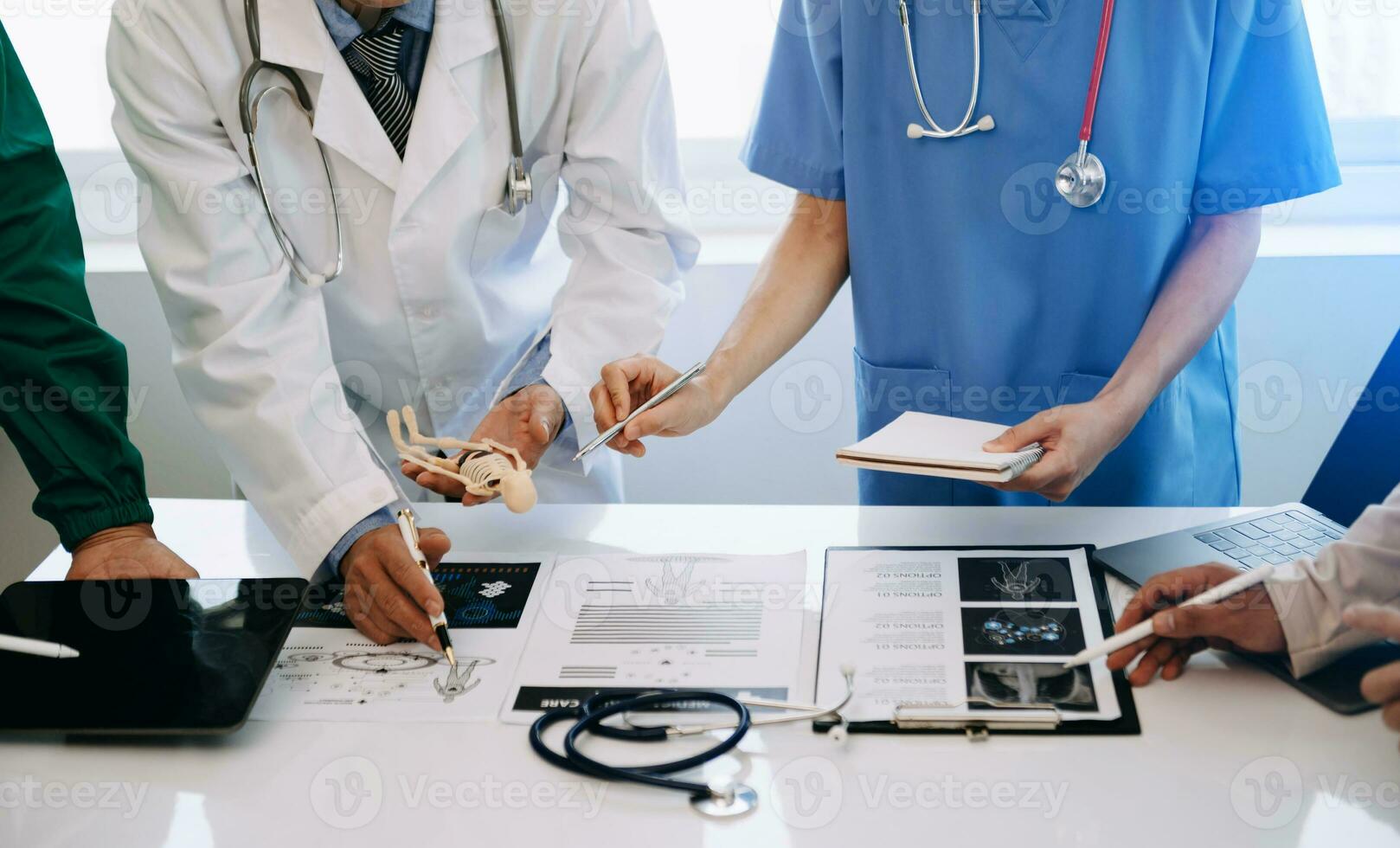 Medical team having a meeting with doctors in white lab coats and surgical scrubs seated at a desk discussing a patients working online using computers in the medical industry photo