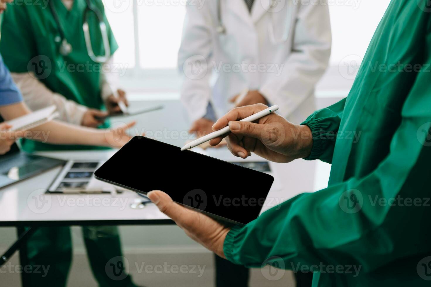 Medical team having a meeting with doctors in white lab coats and surgical scrubs seated at a desk discussing a patients working online using computers in the medical industry photo
