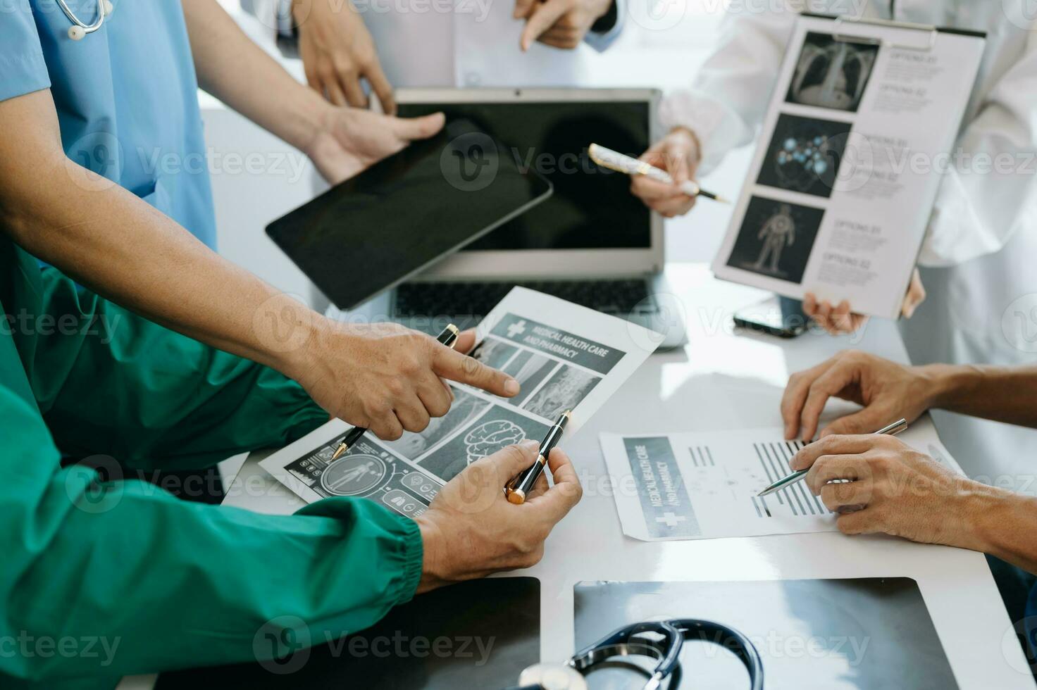 Medical team having a meeting with doctors in white lab coats and surgical scrubs seated at a table discussing a patients working online using computers in the medical industry photo