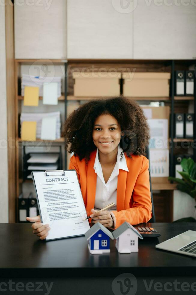 Young real estate agent worker working with laptop and tablet at table in office and small house beside it. photo