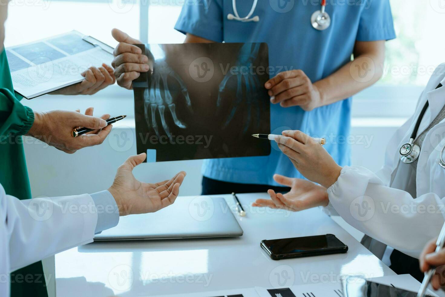 Medical team having a meeting with doctors in white lab coats and surgical scrubs seated at a table discussing a patients working online using computers in the medical industry photo