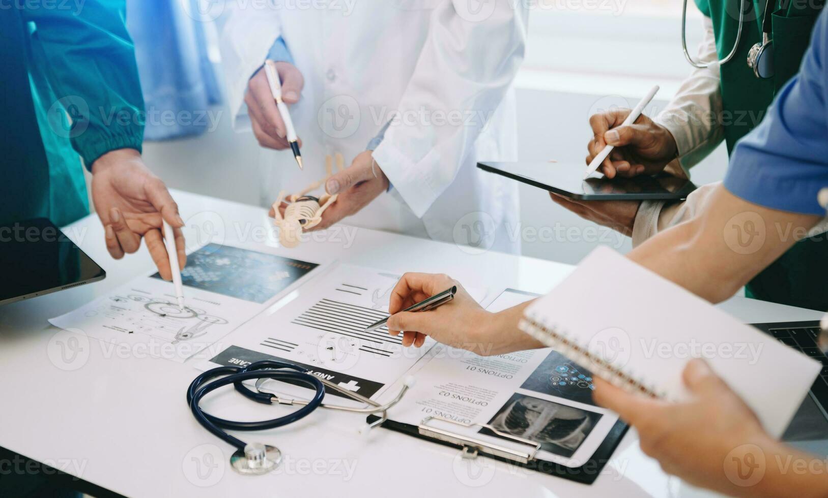 Medical team having a meeting with doctors in white lab coats and surgical scrubs seated at a desk discussing a patients working online using computers in the medical industry photo