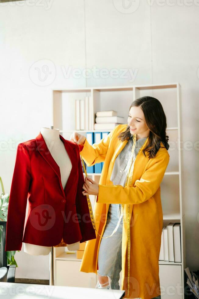 Caucasian young woman on desk in home office of fashion designer and holds tablet, laptop and smartphone. photo