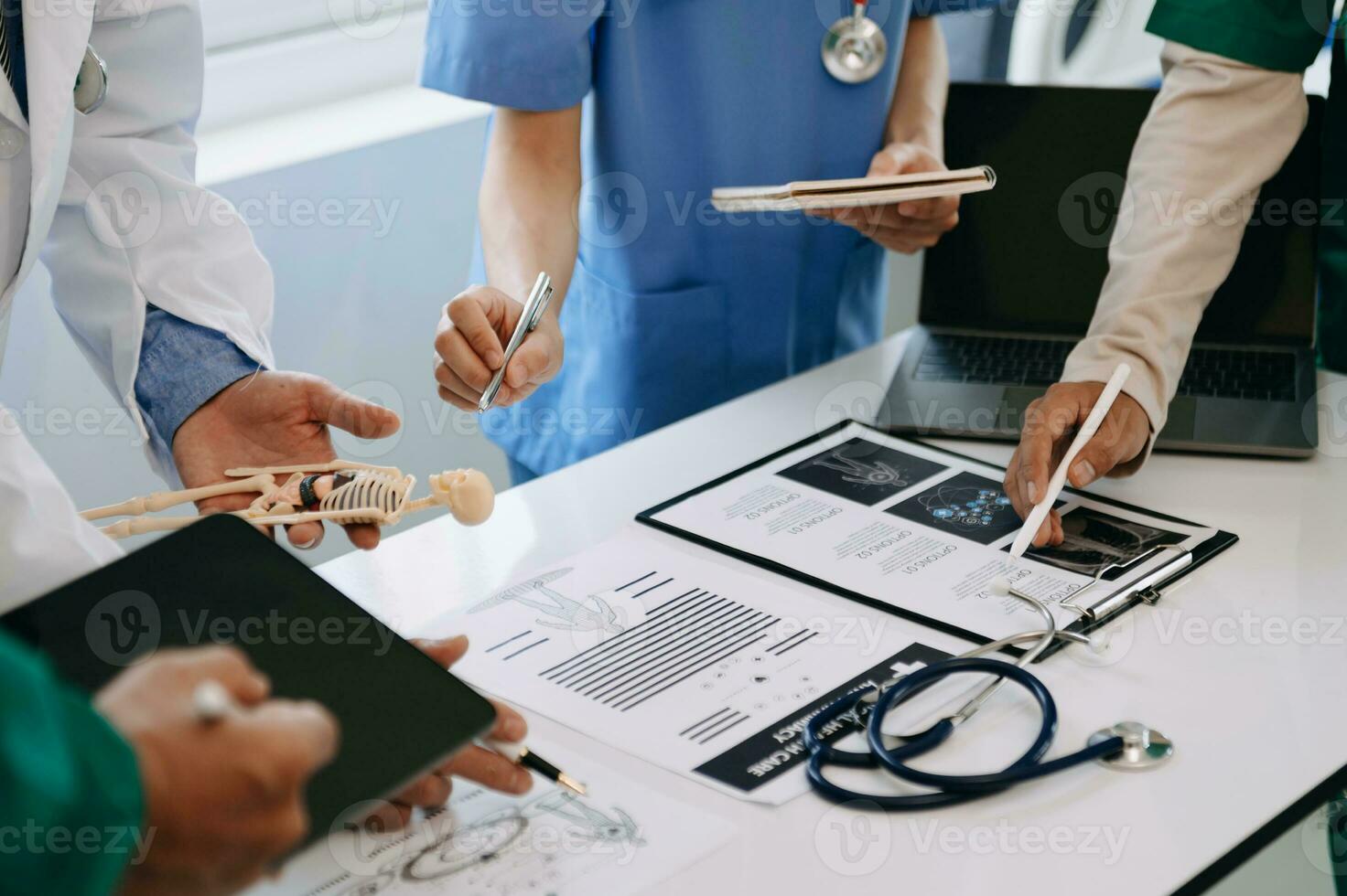 Medical team having a meeting with doctors in white lab coats and surgical scrubs seated at a desk discussing a patients working online using computers in the medical industry photo