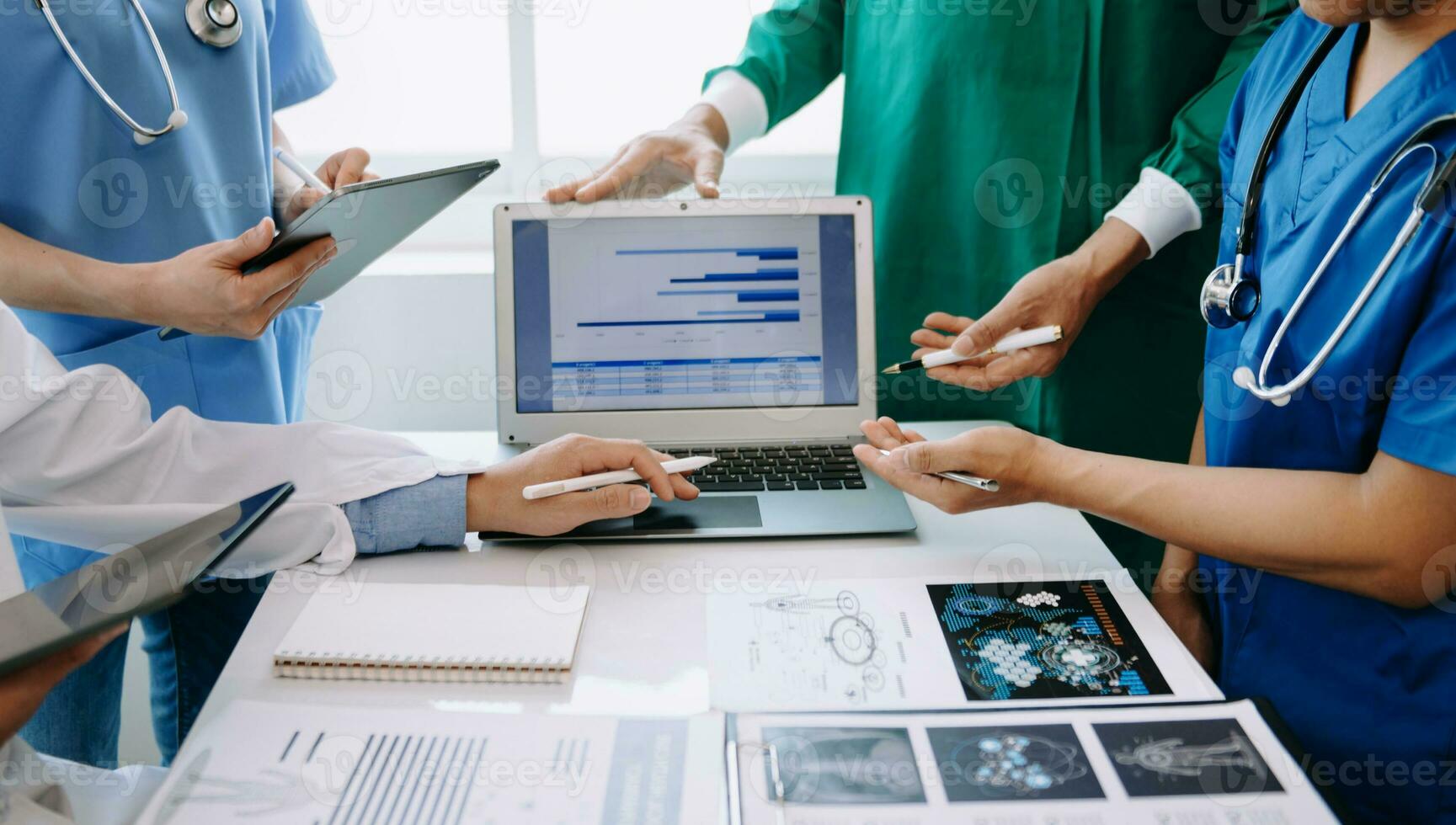 Medical team having a meeting with doctors in white lab coats and surgical scrubs seated at a table discussing a patients working online using computers in medical industry photo