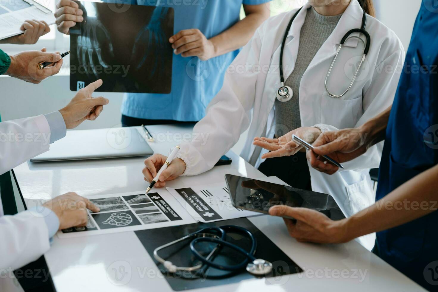 Medical team having a meeting with doctors in white lab coats and surgical scrubs seated at a table discussing a patients working online using computers in the medical industry photo