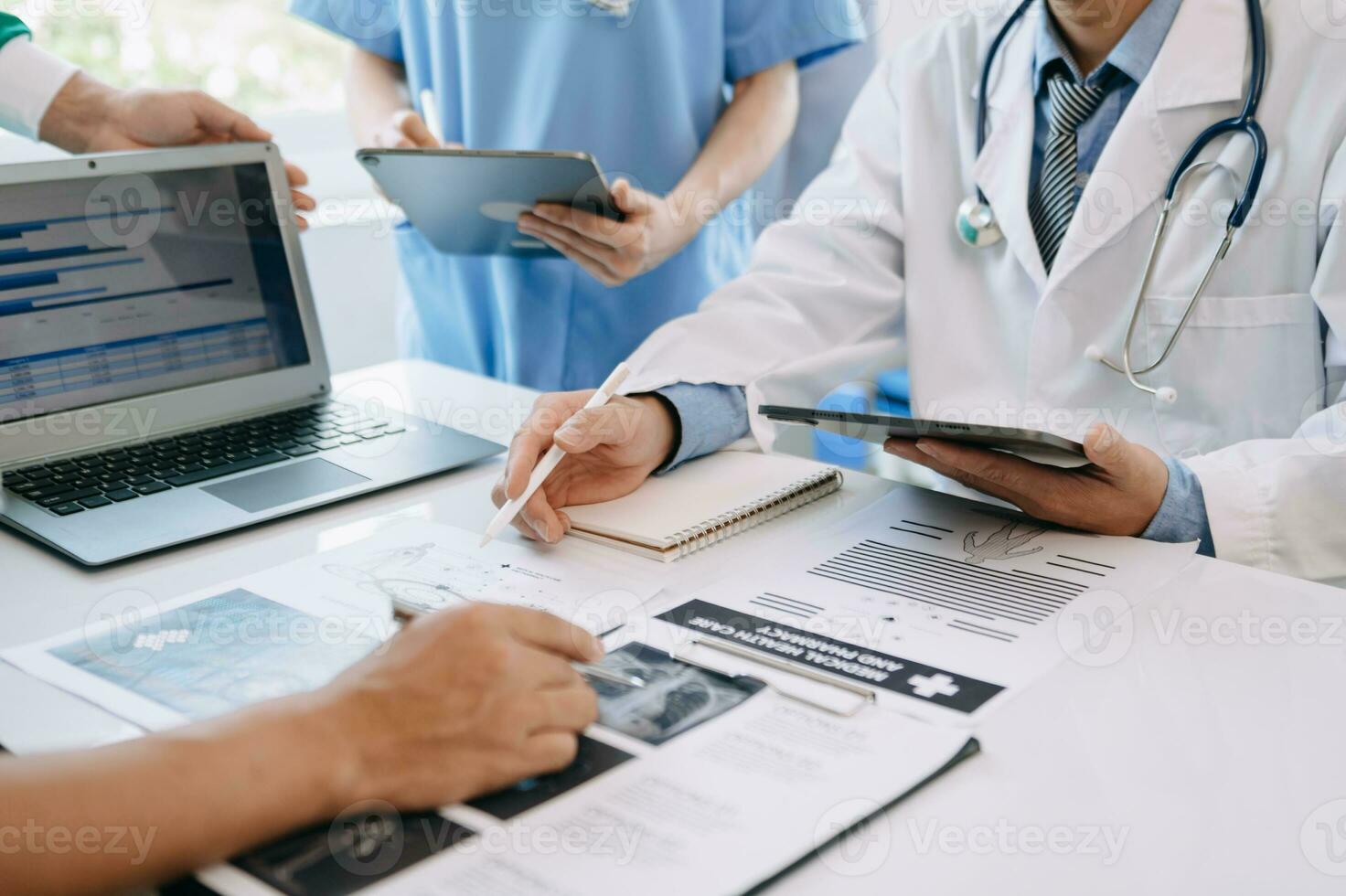 Medical team having a meeting with doctors in white lab coats and surgical scrubs seated at a table discussing a patients working online using computers in medical industry photo