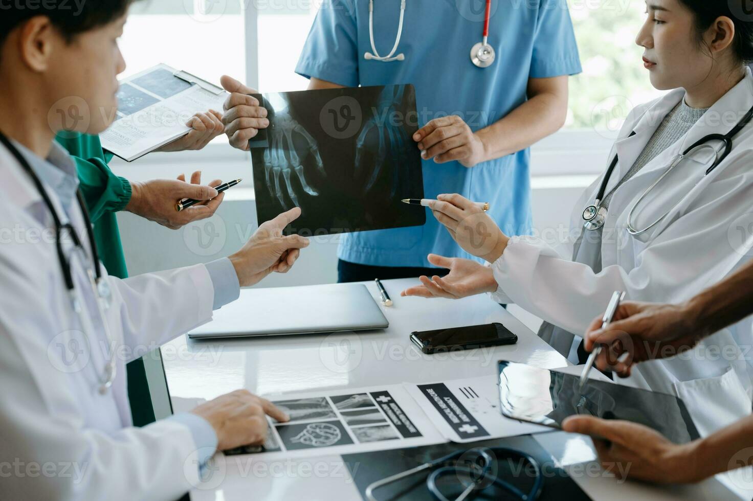 Medical team having a meeting with doctors in white lab coats and surgical scrubs seated at a table discussing a patients working online using computers in the medical industry photo