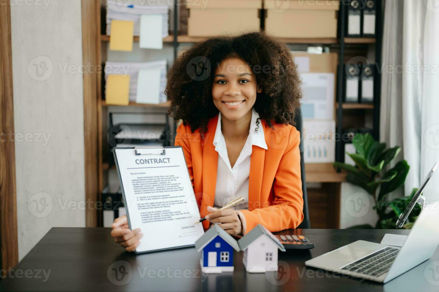 Young real estate agent worker working with laptop and tablet at table in office and small house beside it. photo