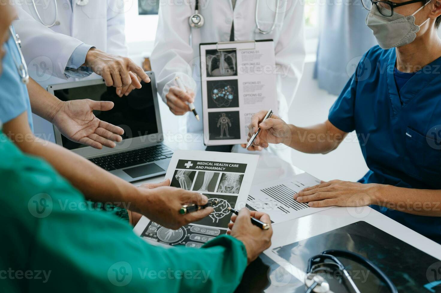 Medical team having a meeting with doctors in white lab coats and surgical scrubs seated at a table discussing a patients working online using computers in the medical industry photo