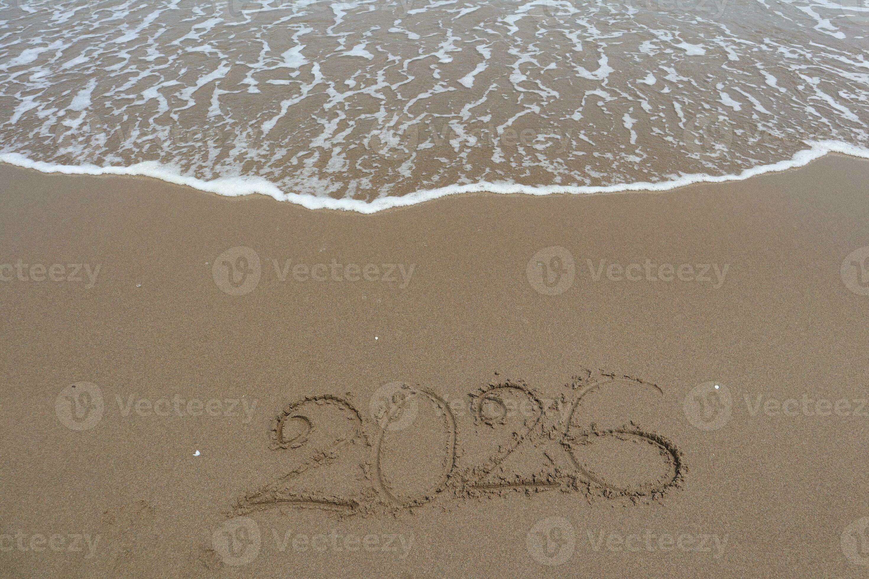 New Year 2026 written in the sand on a beach with sea wave background