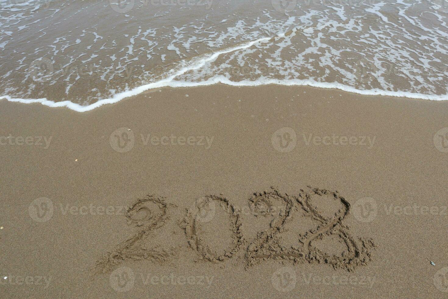 New Year 2028 written in the sand on a beach with sea wave background. photo