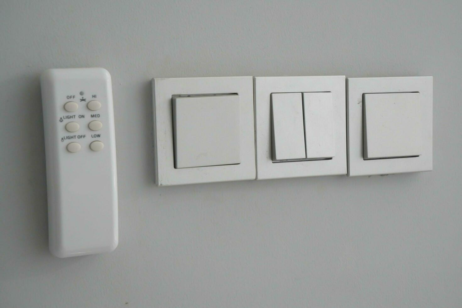 On a gray background, there is a light switch button with an air conditioner remote. AC Remote photo