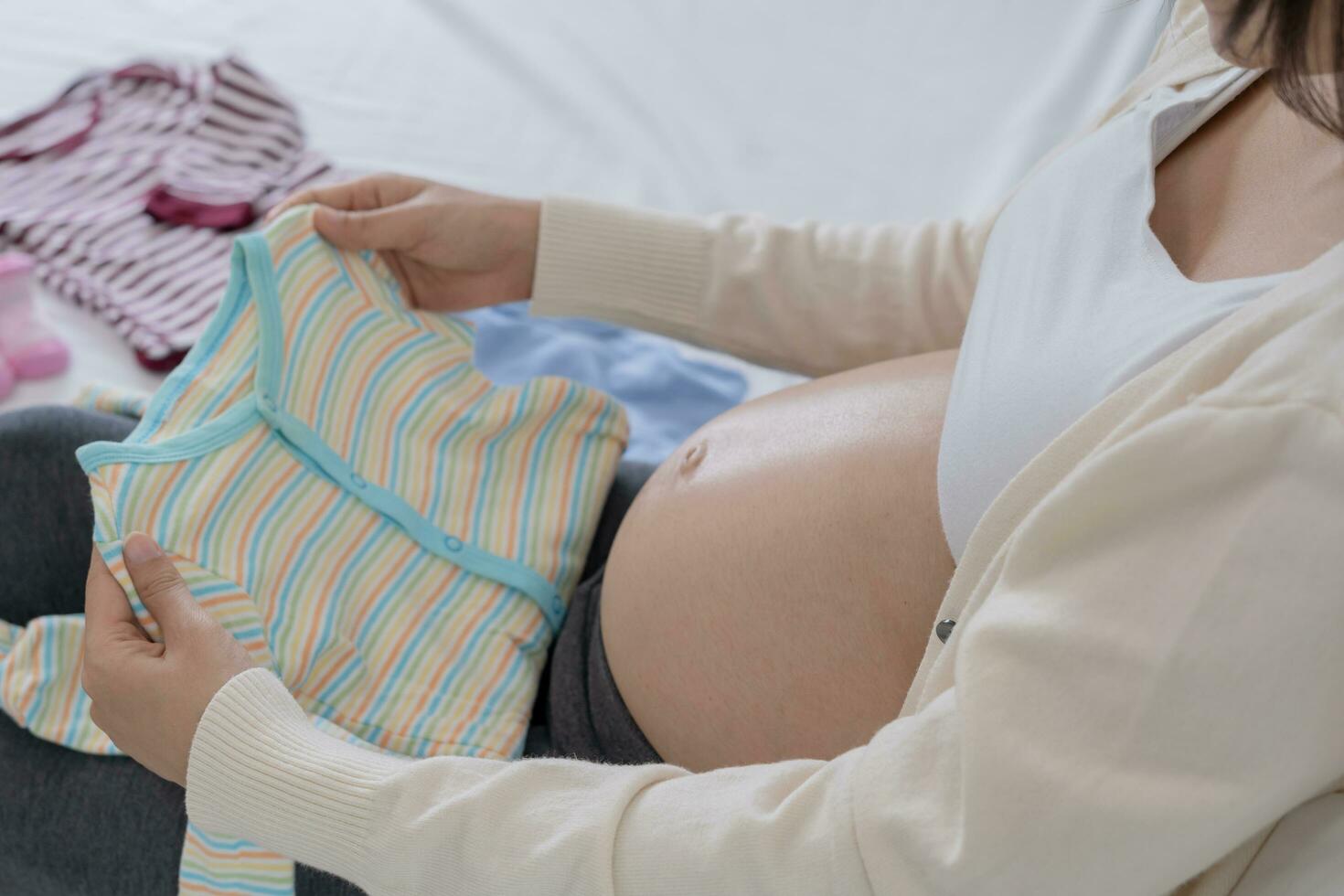 Mother is folding baby clothes to prepare for the upcoming baby. A pregnant woman is checking necessary for newborn. Concept prepare of pregnancy readiness for mothers. photo