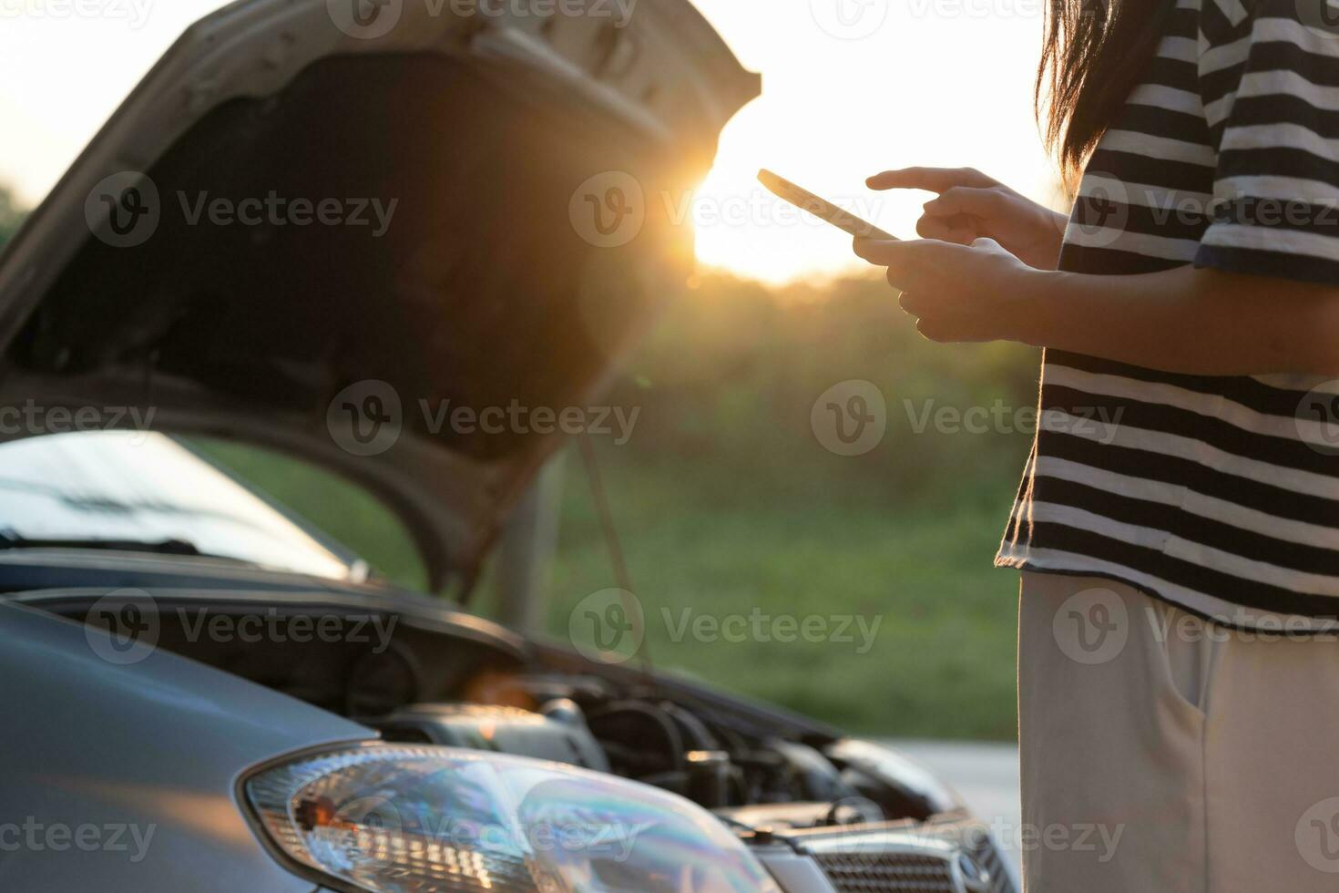 breakdown, broken car, repair. Woman uses mobile phone check insurance premiums through application due to car accident . Find garage to get car fixed during country tour, waiting for help, emergency. photo