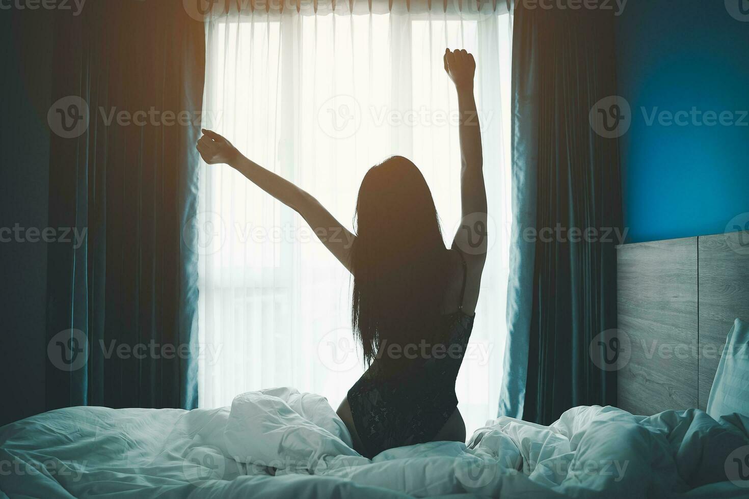 Young asian woman wake up with happy relax look at the window and stretching arms on bed in bedroom interior. woman wake up early in the morning in the cozy bedroom. photo