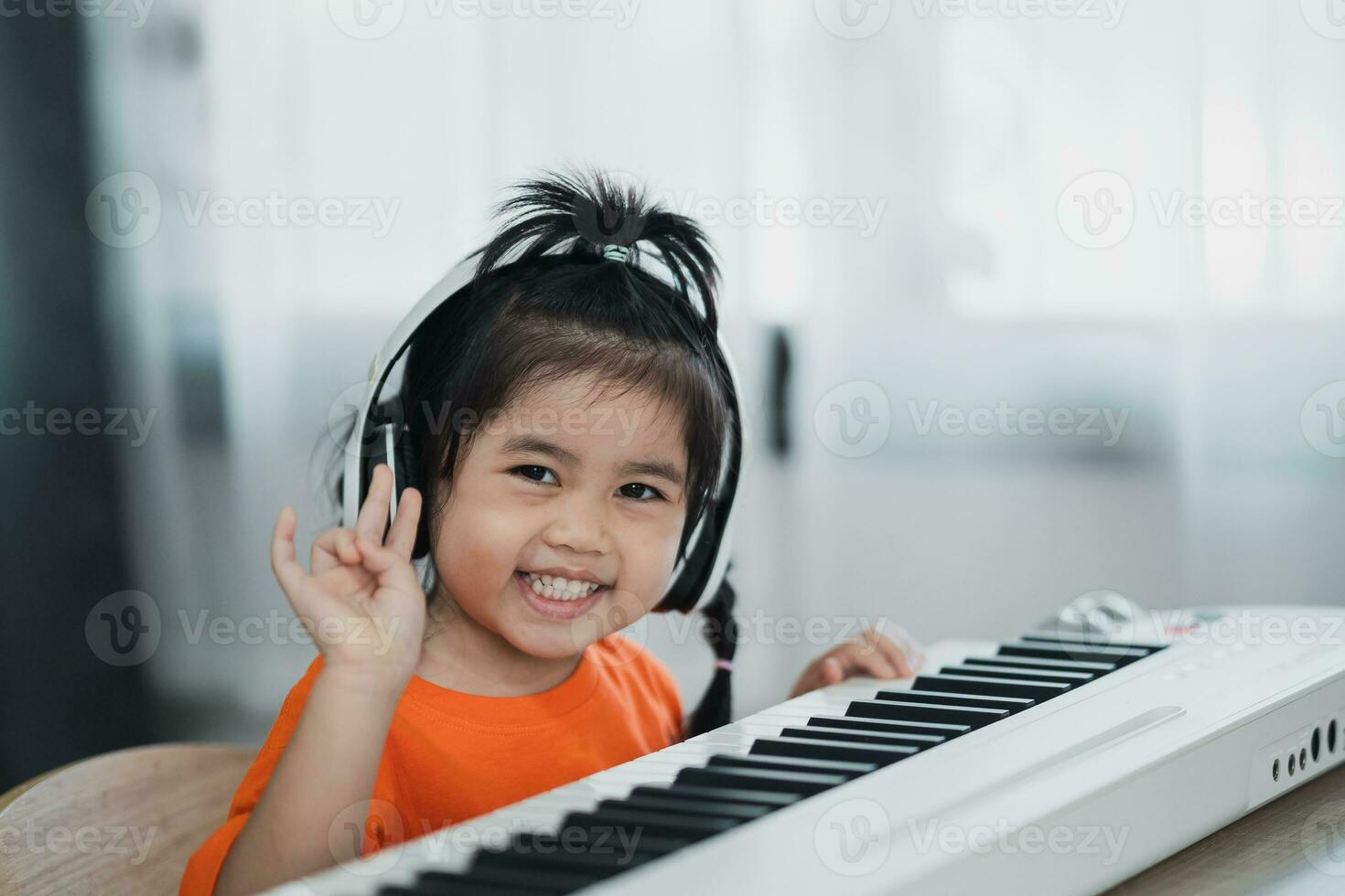 asiático linda niña vistiendo auricular aprendizaje en línea piano música con profesor por móvil teléfono o tableta. el idea de ocupaciones para el niño a hogar durante cuarentena. música aprendizaje estudiar concepto. foto