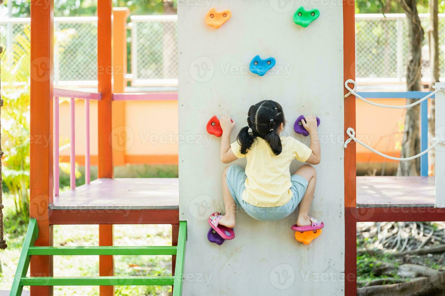 Cute asian girl smile climbing ladder and play on school or kindergarten yard or playground. Healthy summer activity for children. Little asian girl funny happy. Child playing on outdoor playground. photo