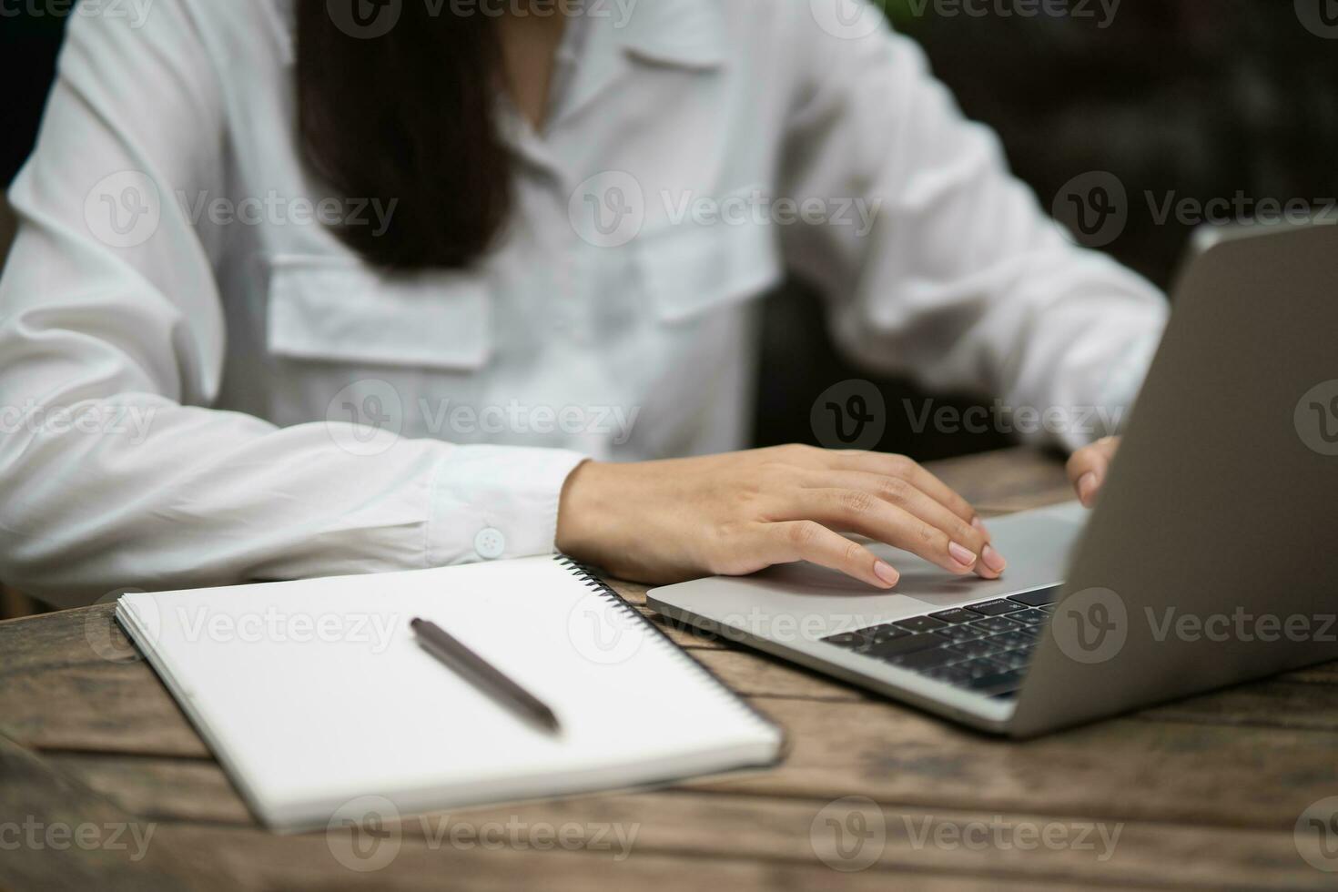 Asian young woman in smart casual wear writing on notebook and working on laptop while sitting in creative office or cafe. young girl working with laptop on the wood table in the cafe photo