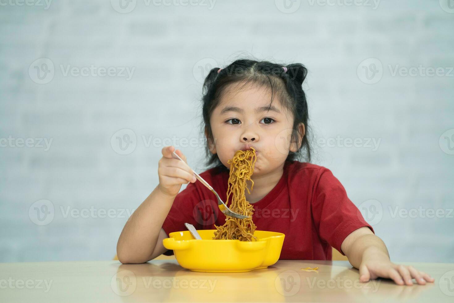 Asian baby girl enjoy happy using cutlery spoon and fork eating delicious noodle in kitchen on dining table. Happy asian baby girl practice eating by her self on dining table. Baby food concept photo