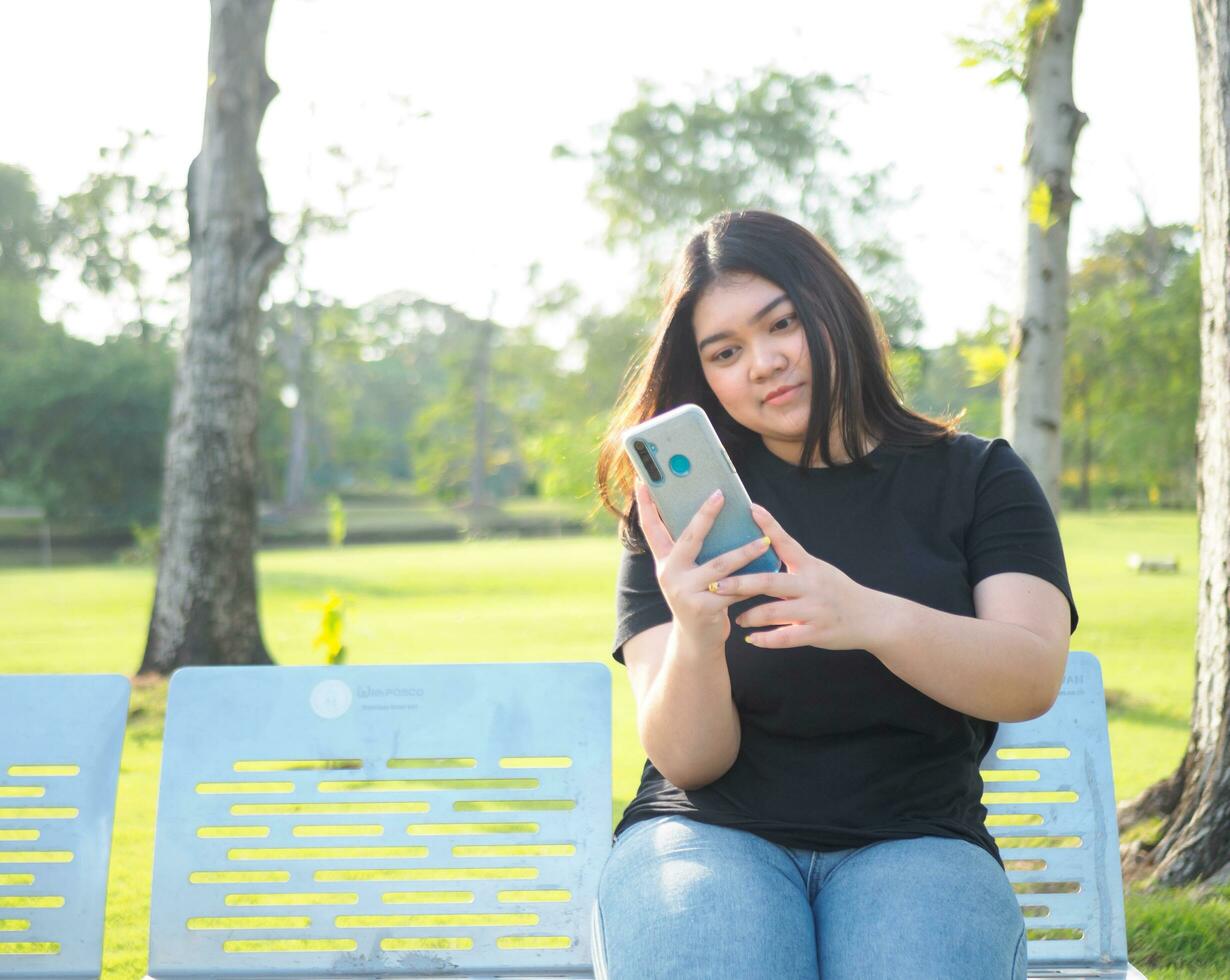 portrait young woman asian chubby cute beautiful one person wear black shirt look hand holding using smart phone in garden park outdoor evening sunlight fresh smiling cheerful happy relax summer day photo