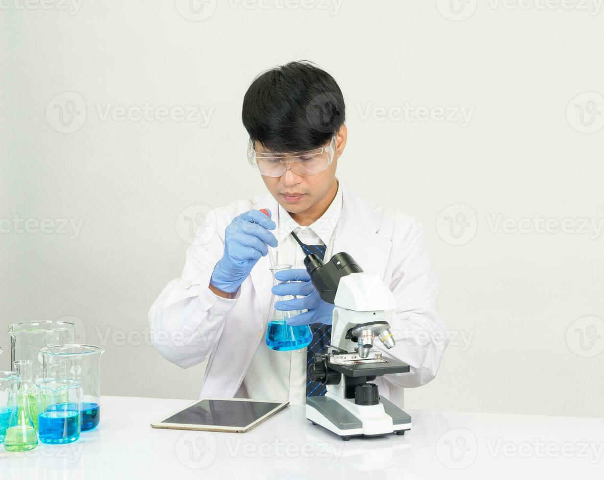 asiático masculino estudiante científico vistiendo un del doctor vestido en el laboratorio mirando a el químico. causado por mezcla reactivos en científico investigación laboratorios con prueba tubos y microscopio en el mesa foto