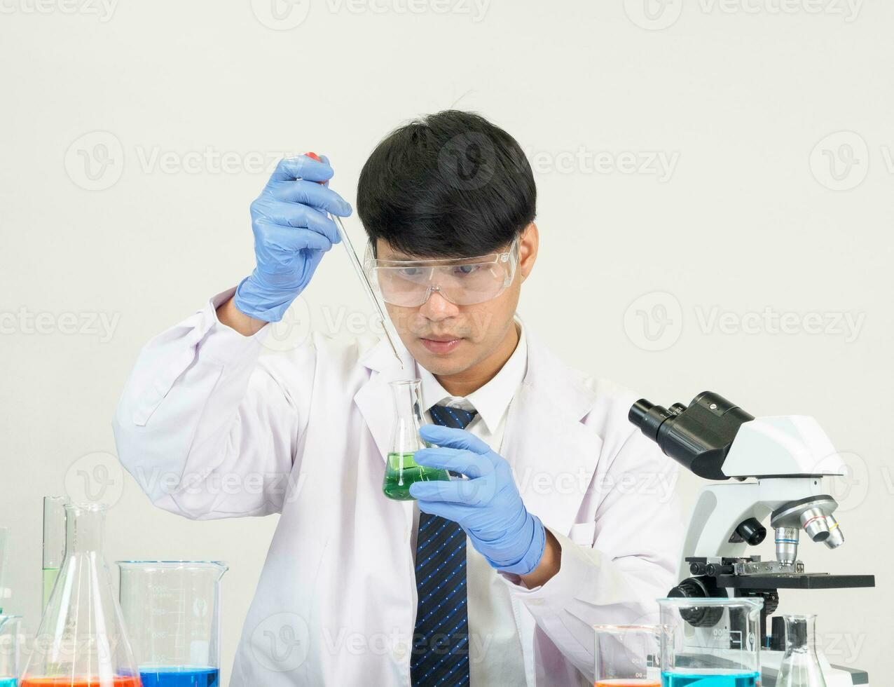 Asian male student scientist Wearing a doctor's gown in the laboratory, looking at the results through a microscope. on a table in a scientific research laboratory with test tubes on a white table photo