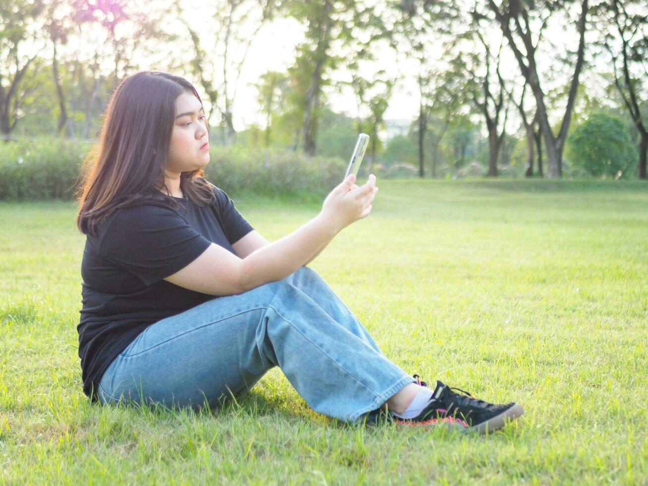 Portrait young woman asian chubby cute beautiful one person wear black shirt look hand holding using smart phone in garden park outdoor evening sunlight fresh smiling cheerful happy relax summer day photo
