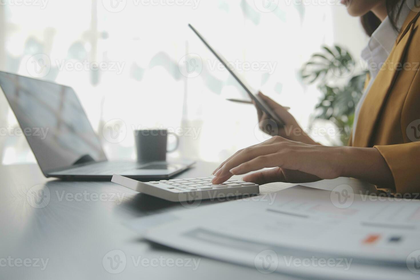 Asian Business woman using calculator and laptop for doing math finance on an office desk, tax, report, accounting, statistics, and analytical research concept photo