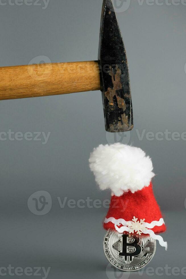 Bitcoin in a Santa Claus hat and a hammer on a gray surface. photo
