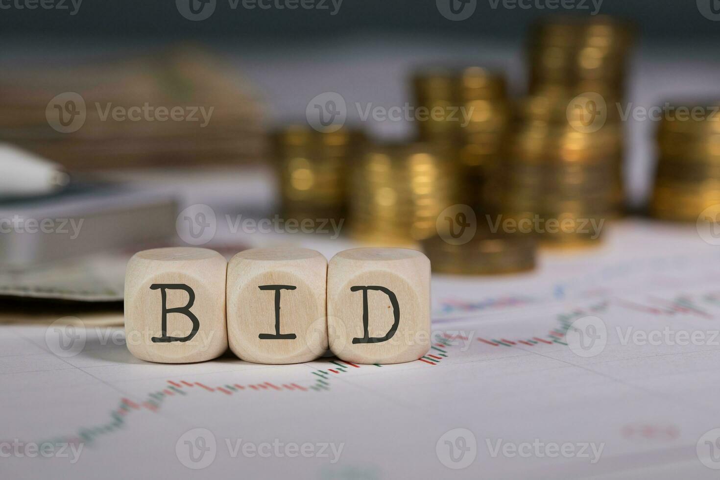 Word BID composed of wooden letter. Stacks of coins in the background. photo